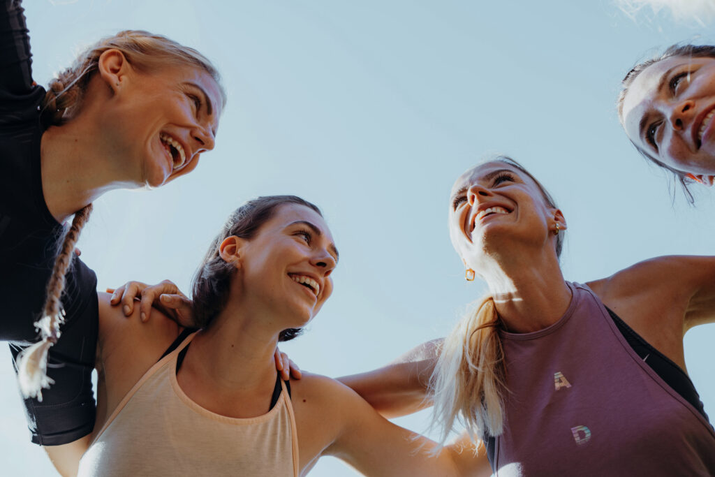Intervalltraining – vier Frauen schauen strahlend nach oben, feiern gemeinsam nach intensiver Trainingseinheit, Teamgeist pur