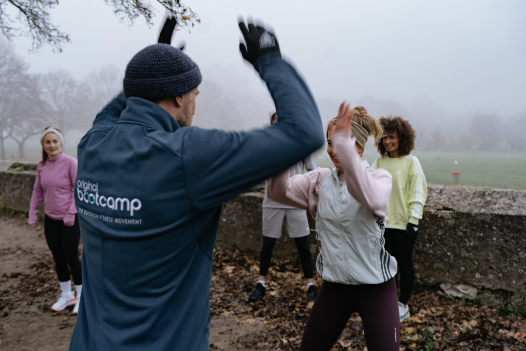 Intervalltraining – Original Bootcamp Trainer gibt High-Five an Läuferin, Team jubelt beim Intervall-Training, Feldtraining