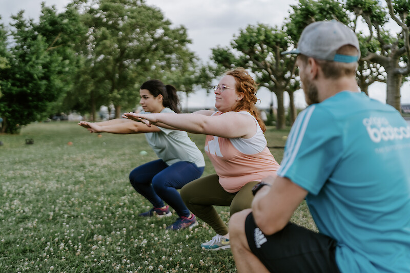 Neujahr Fitness: Funktionelles Gruppentraining im Park mit Kniebeugen – gemeinsames Outdoor-Workout für Kraft, Stabilität und Motivation.