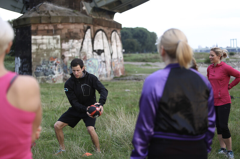 Outdoor-Fitness Einheit mit Medizinball unter Anleitung eines Trainers im Park.