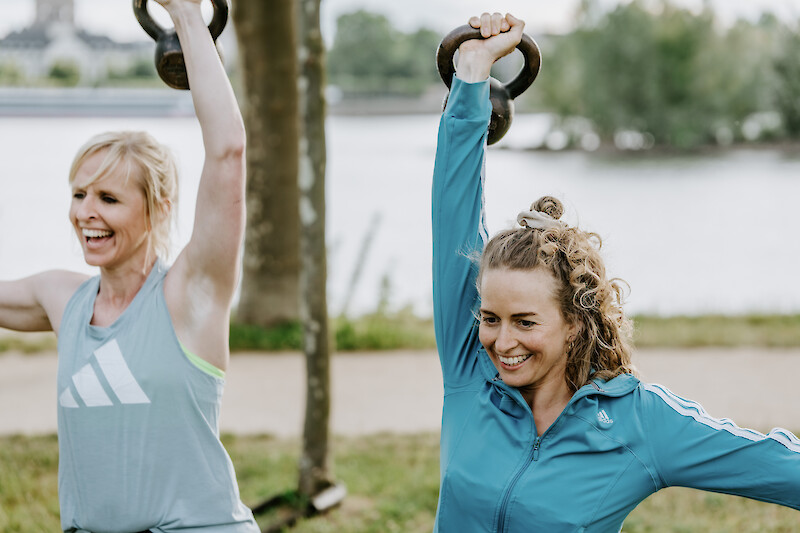 Zirkeltraining Outdoor: Zwei Frauen trainieren mit Kettlebells am Wasser.
